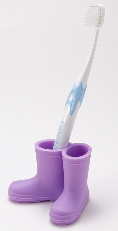 紫色のレインブーツ型歯ブラシホルダーに立てられた、コンパクトヘッドの白い歯ブラシ