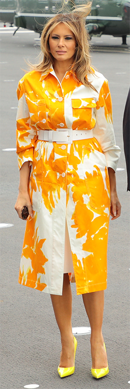 白地にオレンジ色の大きな花が描かれたコートを着たメラニア夫人