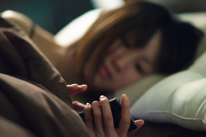 ベッドでスマートフォンに夢中になっている女性