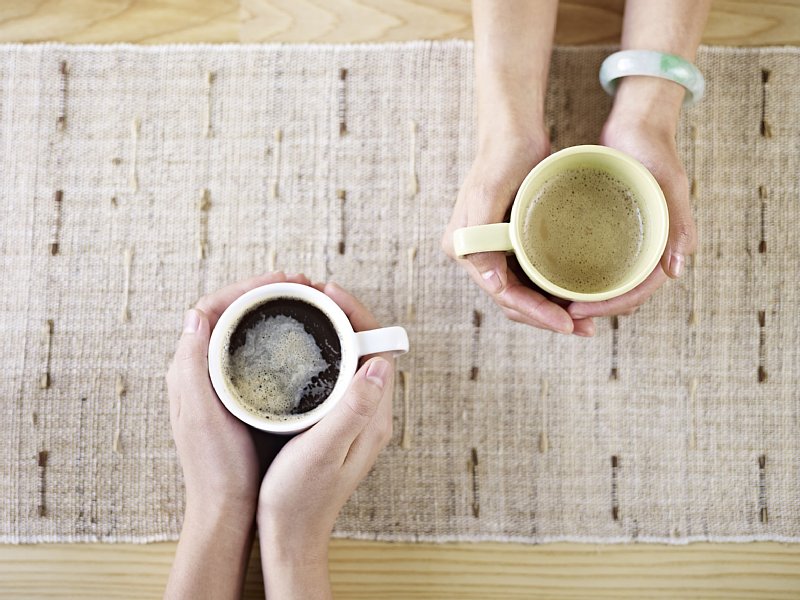 コーヒーの入ったカップに両手を添えている写真
