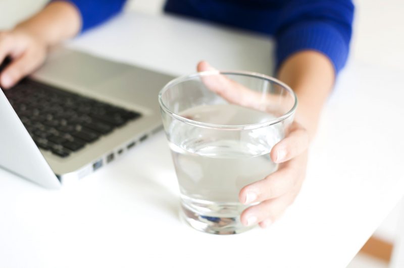 水のグラスを手にした女性の手元とパソコンの画像