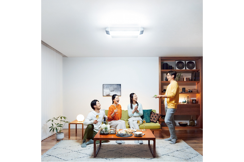 パナソニック『AIR PANEL LED THE SOUND HH-XCF1203A（LINK STYLE LED対応）』のLED照明が明るめでついているリビングと男性2人と女性2人でホームパーティをしている様子