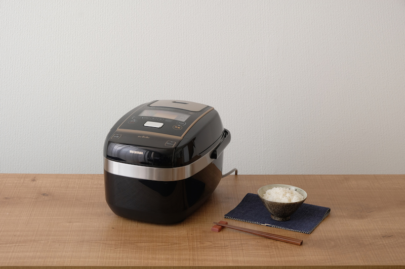 アイリスオーヤマ　『銘柄量り炊き 圧力IHジャー炊飯器5.5合　KRC-PC50-B』の隣に茶碗に入ったご飯と箸