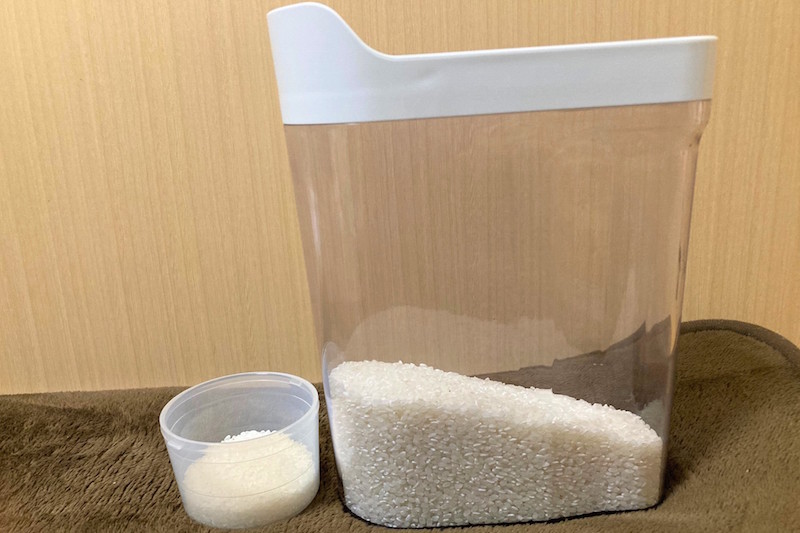 米が1／4入った無印良品の冷蔵庫用米保存容器と米が入った専用の計量カップ