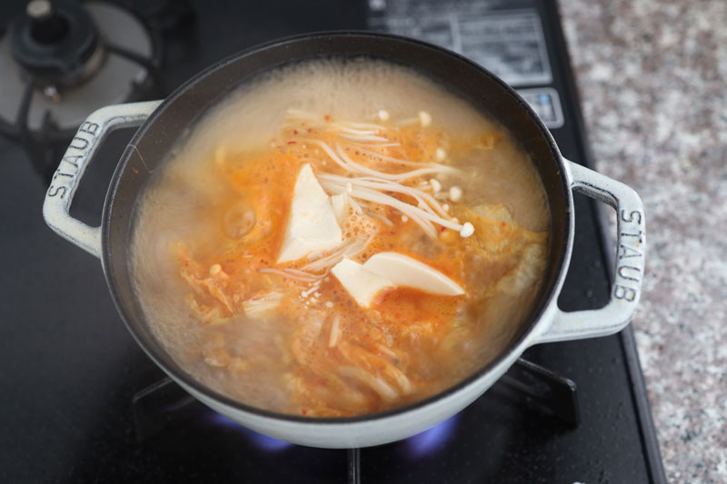 【A】を加えて一煮立ちさせたら、えのきたけを石付きをとってほぐし、鍋に入れる。豆腐はスプーンですくいながら加える