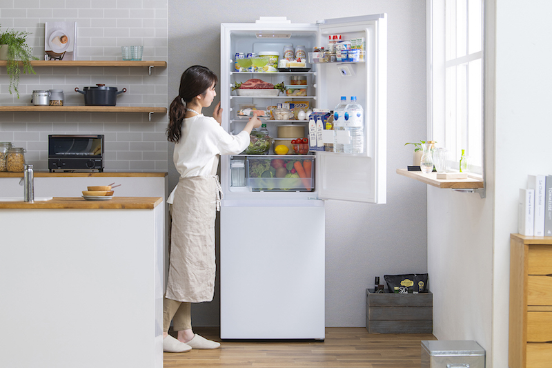 アイリスオーヤマ『STOCK EYE カメラ付き冷凍冷蔵庫 296L』 ※中容量・右開きタイプ のドアを開け食材に手を伸ばしている女性