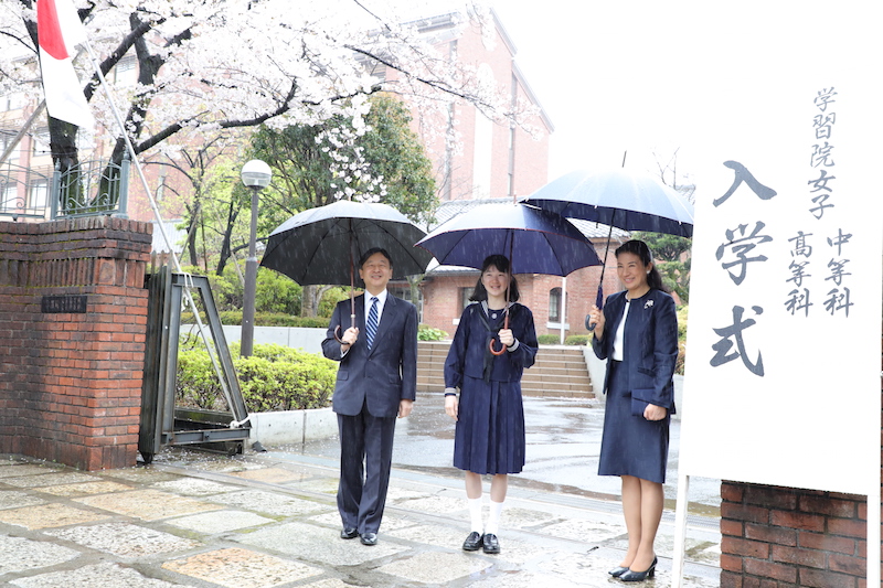 傘を指し2017年4月、愛子さまの学習院女子高等科の入学式にご出席される天皇皇后両陛下と愛子さま後ろには桜が咲いている
