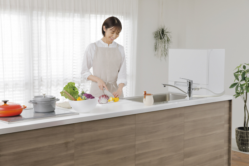 パナソニック『食器洗い乾燥機 スリム食洗機　NP-TSK1』がキッチンのシンク横においてあり、女性が野菜を切っている
