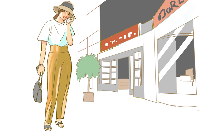 白いTシャツに茶色のパンツ、帽子をかぶりサンダルを穿いた女性が街なかに立っているイラスト