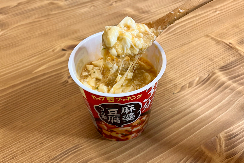 カップ de クッキング 麻婆豆腐の素にオートミールや豆腐やチーズを加えたものをスプーンですくっている