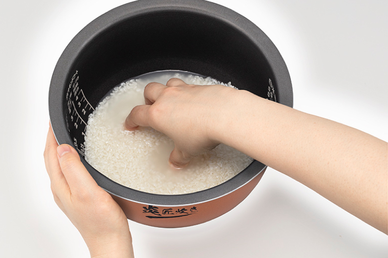 東芝の炊飯器の内釜で米を研ぐ人の手元