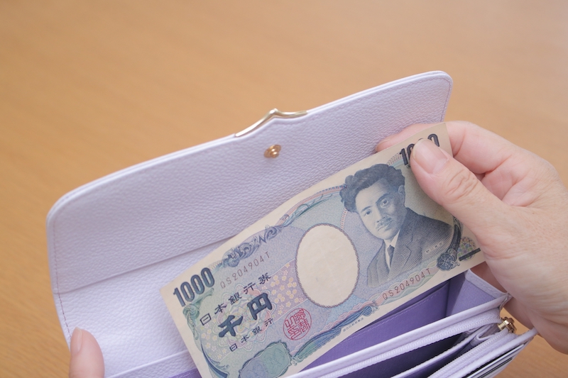 紫の財布から千円札を出している