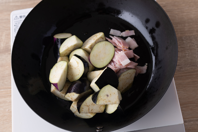 大きめのフライパンでオリーブオイルとにんにくを弱火で熱し、香りがたったらなすとベーコンを加え、中火で炒める