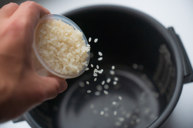 炊飯器に計量カップのお米を入れている手元