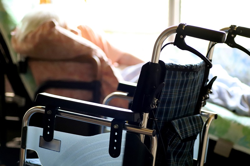 介護ベッドでリクライニングして横たわる高齢女性と車椅子