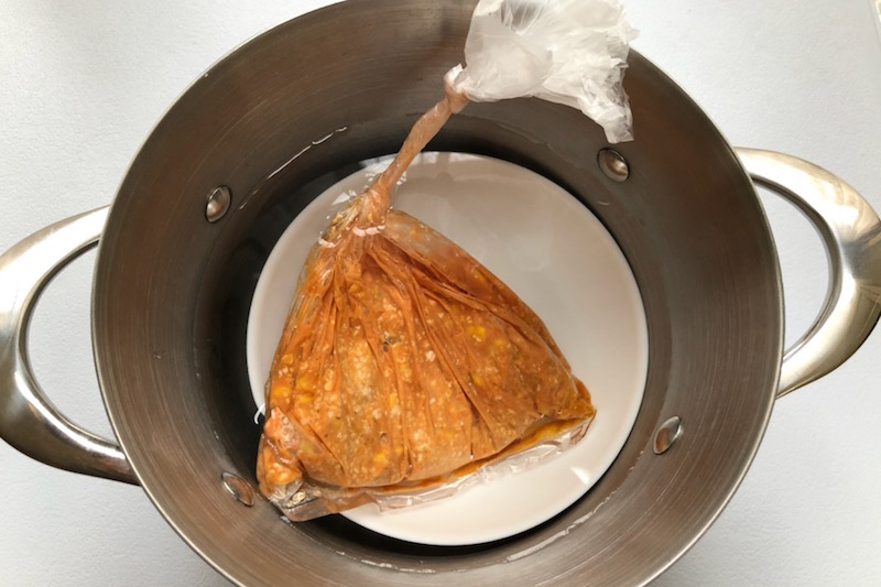 オートミールとドライサラミとコーンドライパックを耐熱性の高密度ポリエチエン製のポリ袋に入れ混ぜ、湯煎する様子