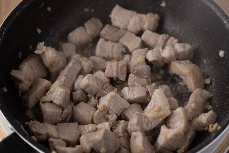 フライパンでサラダ油を中火で熱し、豚バラ肉を炒めにんにく、しょうがを加える
