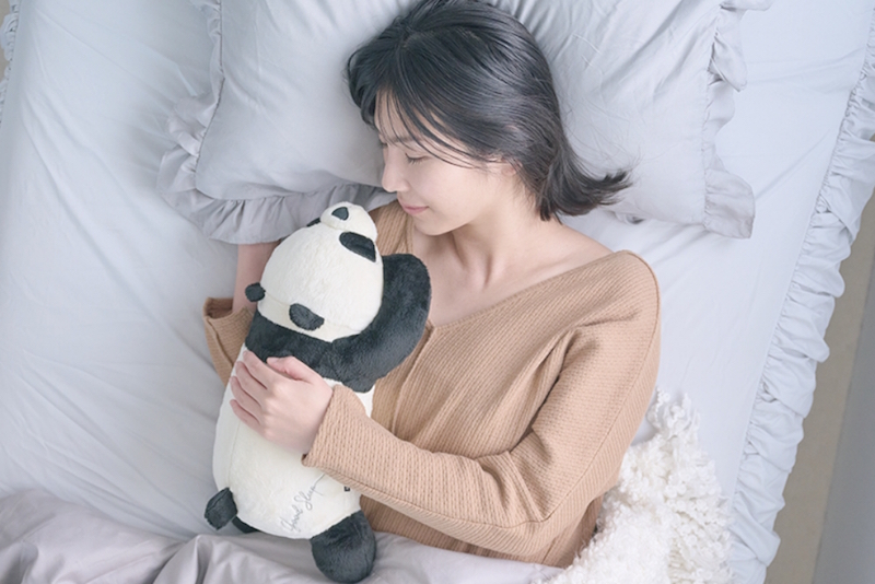 パンダのぬいぐるみを抱いて寝る女性