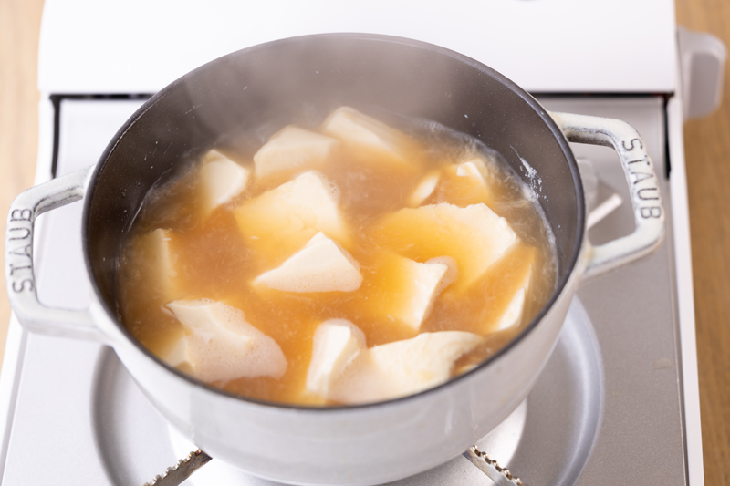 豆腐をスプーンですくい入れる。鍋を中火で熱し、沸騰したら2、3分煮込む